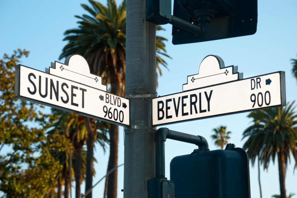 Street signs of the intersection of Sunset Boulevard and Beverly Drive with palm trees in the background